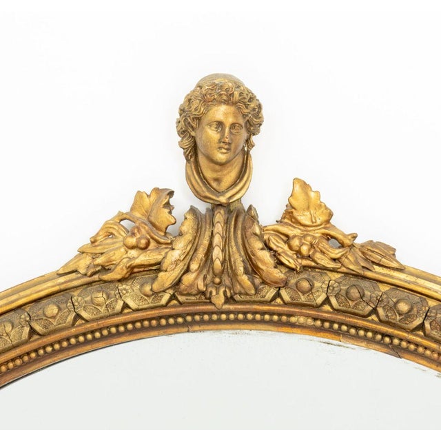 Neoclassical Style Giltwood Framed Oval Mirror, with male bust form crest. Mirror plate: 49.25" H x 38.5" W; frame: 58" H...