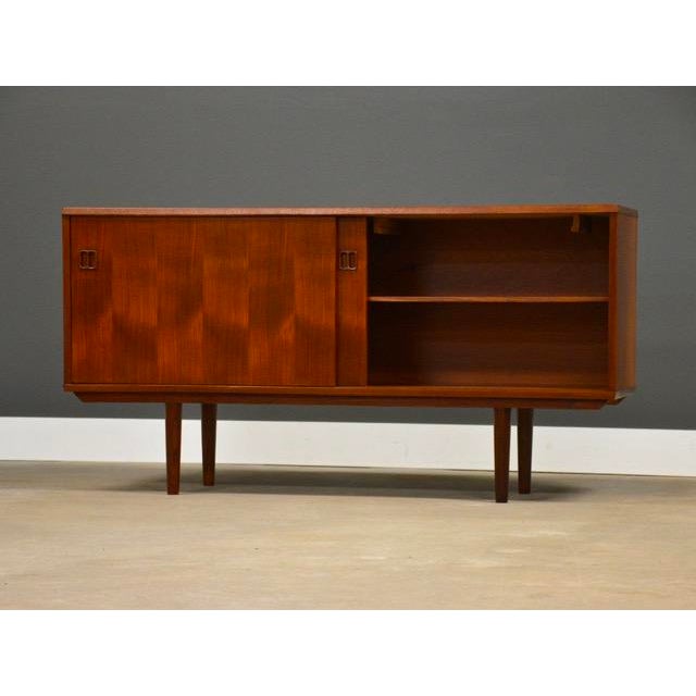 A mid century modern teak credenza with two sliding doors, two shelves and tapered legs. Professionally refinished....