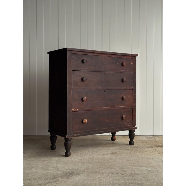 Antique pine chest of drawers with four graduated drawers and turned wooden feet. Retains its original dark painted...