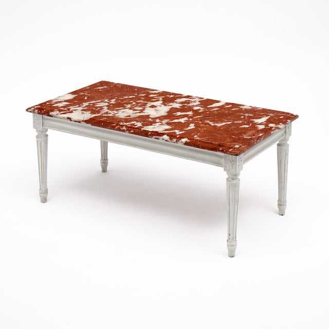 A refined French Louis XVI style coffee table, distinguished by its richly veined Rouge Royal marble top in warm red,...