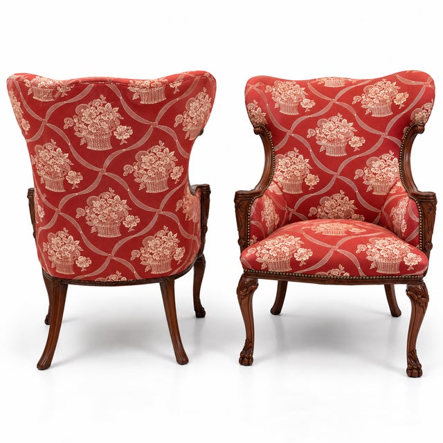 This is a pair of antique French carved mahogany wing chairs in a vintage Schumacher red and white fabric. They have brass...