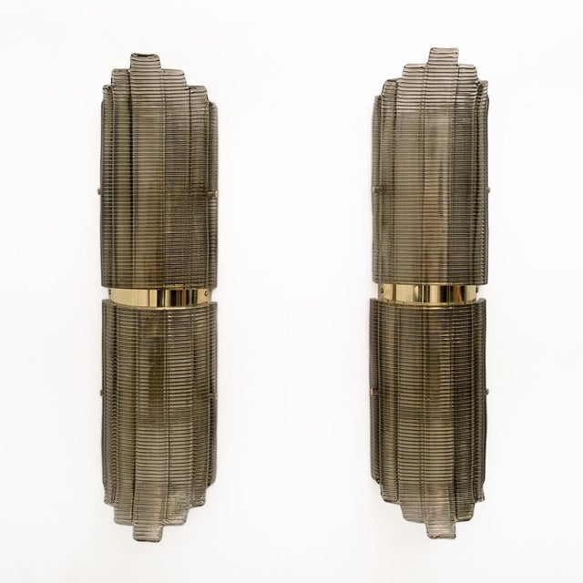 A pair of smoke-colored Murano glass wall sconces in textured glass and brass. The ribbed glass is curved in design,...