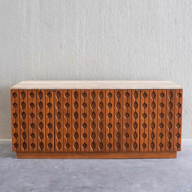This is a sideboard executed in the Brutalist style, featuring a carved wood body and a solid travertine top. The piece is...