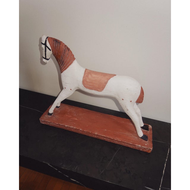 Hand carved folk art horse sculpture in painted wood, featuring an elongated silhouette with carved mane and saddle...