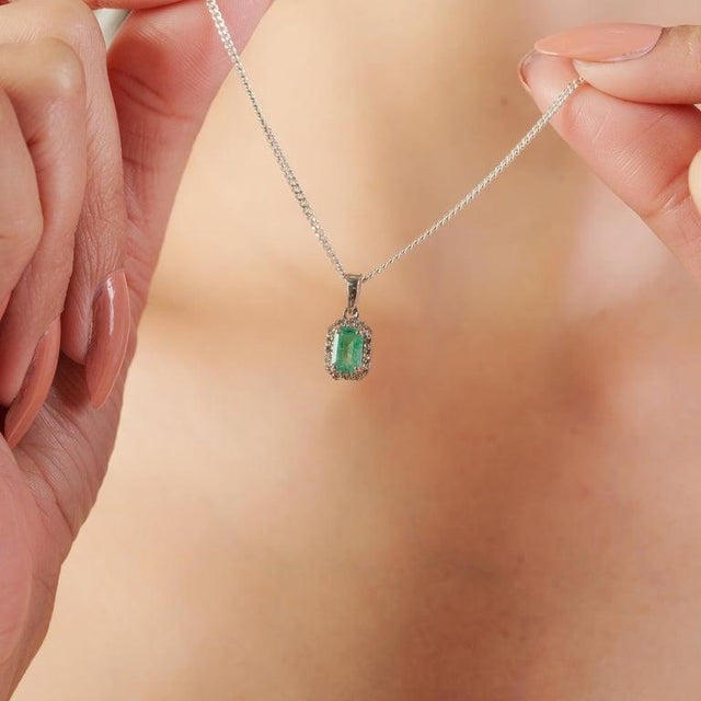 A refined halo pendant featuring a rectangular emerald set totalling 0.57 carats, framed by 1 mm diamonds in 925 sterling...