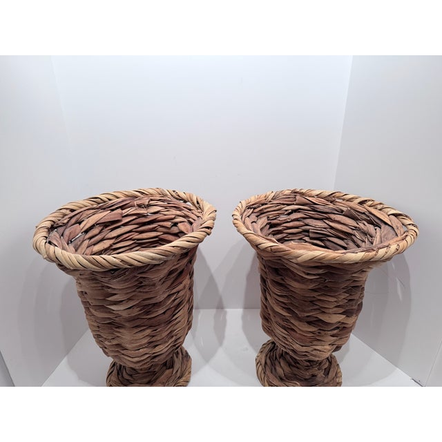 Vintage pair of hand-woven wicker/rattan/seagrass urn-style pedestal vases featuring a flared, braided rim and a footed...