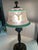 This vintage signed Pairpoint lamp shade with an ornate bronze base features a unique reverse painted design in shades of...