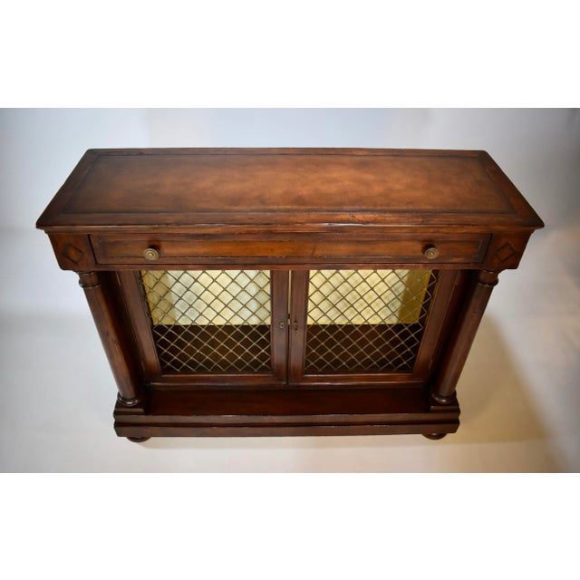 A stately Regency bookcase cabinet with gilt tooled leather top above a single drawer. Two pierced brass lattice trellis...