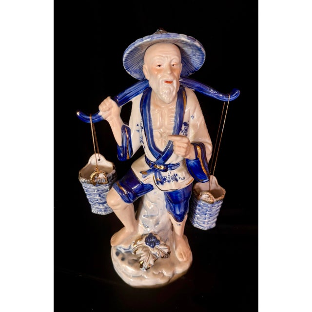 This large figurine depicts a traditional Chinese fisherman wearing a conical hat and carrying water buckets suspended...