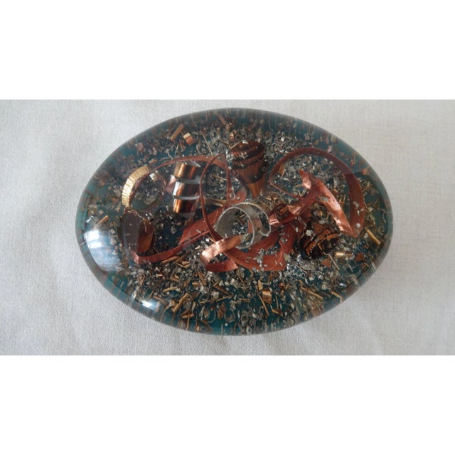 An interesting vintage oval shaped paperweight with various shaped industrial metal shavings from copper, brass and...