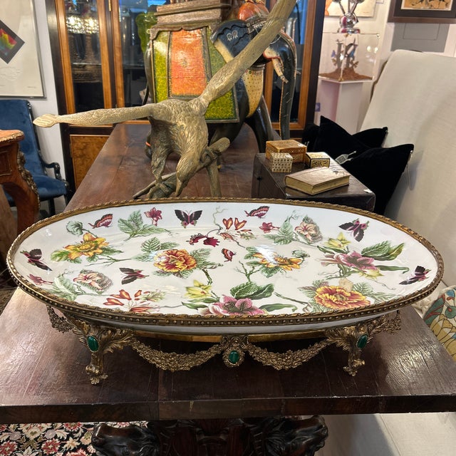 Oblong platter with floral pattern mounted on a metal base. The rim of the decorative platter has metal beading and rope...