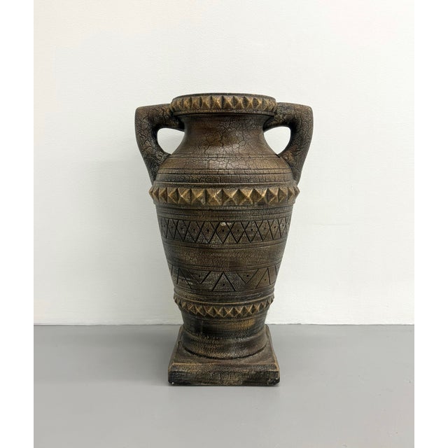 Architectural ceramic urn featuring a substantial handled silhouette with raised geometric banding and a richly textured...