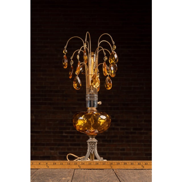 Hollywood Regency table lamp featuring a sculptural amber glass font mounted on an ornate cast-metal base with a white...