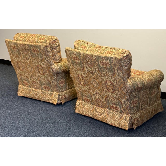 A handsome pair of Jessica Charles swivel chairs upholstered in a richly patterned tapestry of muted gold, sage, and rust....
