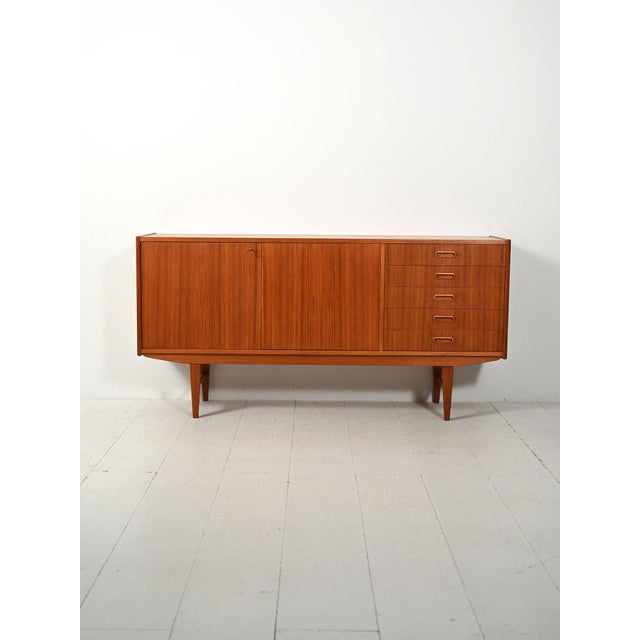 Scandinavian teak sideboard with simple lines, sliding doors, and a row of drawers with carved oval handles. Scandinavian...
