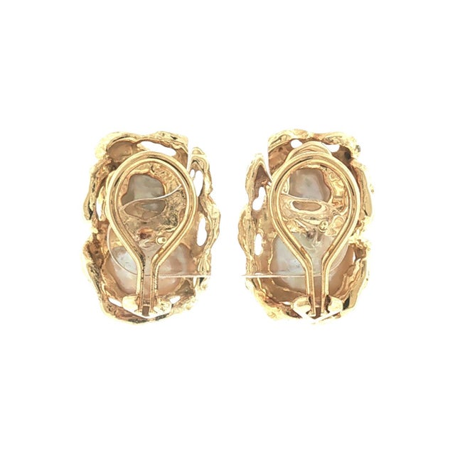 A pair of mid-century brutalist earrings featuring white baroque pearls set in 18k yellow gold. The design showcases an...