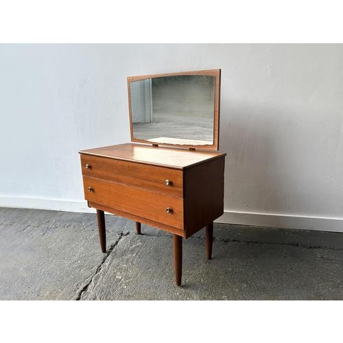 A compact and petite Mid-Century chest of drawers with mirror in rich-toned wood, supported on turned teak legs. It has...