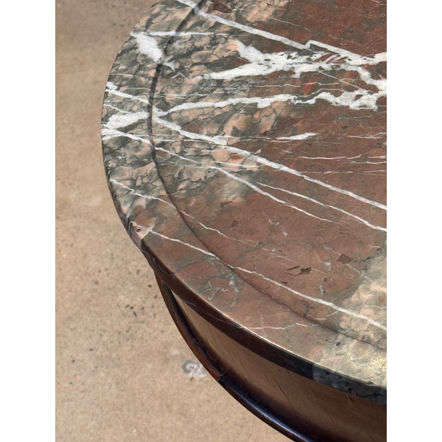 French walnut table with a circular marble top in mottled red and grey with white veining, set within a moulded frieze....