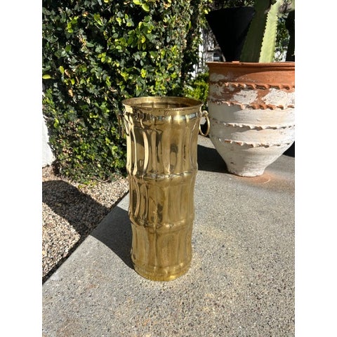 Vintage brass umbrella stand with flared top and tapered cylindrical body. Features two side ring handles and vertically...