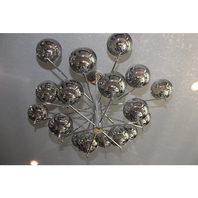 The Donghia Renaldo 18-Arm Chandelier features a luxurious design with grey glass globes and a polished chrome finish,...