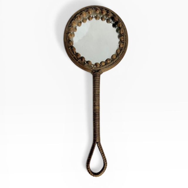 A charming vintage hand mirror featuring a beautifully detailed wicker-wrapped frame and handle. The round mirror is...