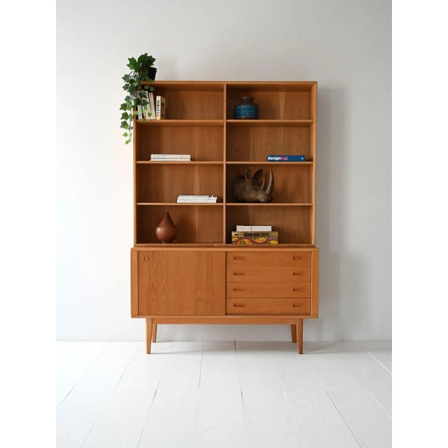 1960s bookcase with open shelves, drawers, and a storage compartment. Linear structure and light proportions typical of...
