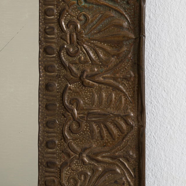 A decorative Arts & Crafts mirror featuring a hand-worked copper frame with repoussé detailing. The textured metal surface...
