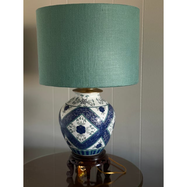 A striking pair of vintage chinoiserie ceramic ginger jar lamps featuring cobalt blue motifs with soft teal accents on a...
