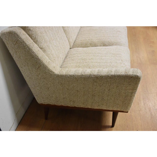 This modern beige sofa designed by Milo Baughman for James Inc. Furniture has a walnut base with canted and tapered back...