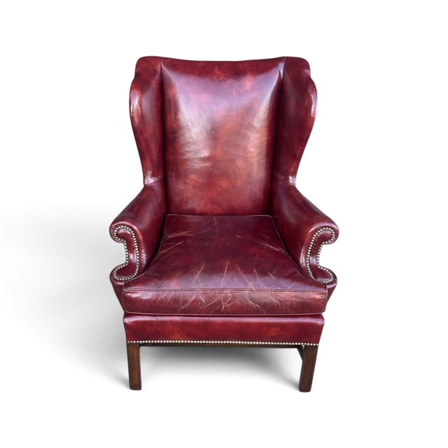 This Baker wingback chair features rich burgundy leather upholstery, a tall back, and classic rolled arms. Brass nailhead...