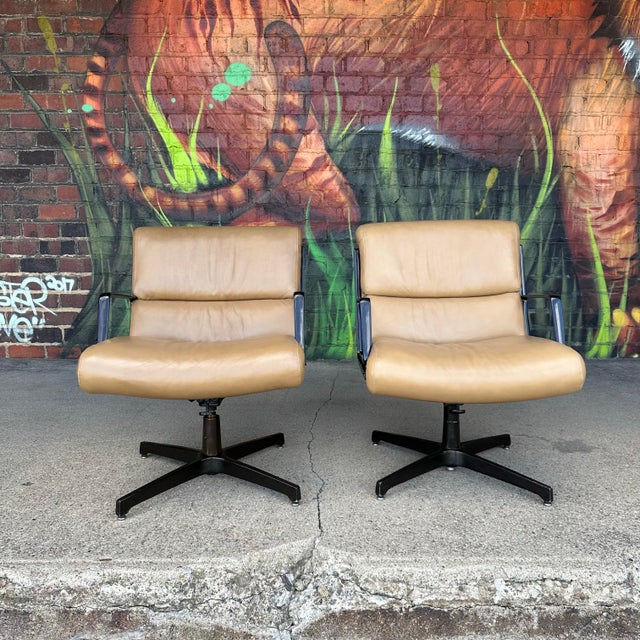Pair of brown leather swivel office chairs on a black metal base/frame. Believed to be designed by Alfred Kill. Seat...
