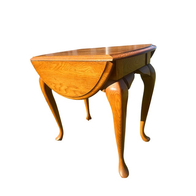 A classic pair of solid oak drop-leaf end tables featuring elegant Queen Anne cabriole legs and a warm, honey-golden...