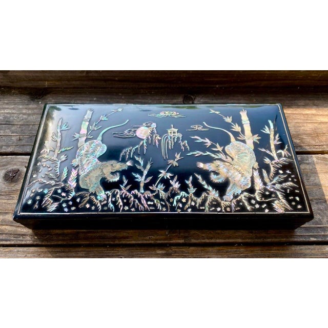 A striking Korean black lacquer smoking box dating to approximately the late 1940s–1950s, richly decorated in hand-cut...