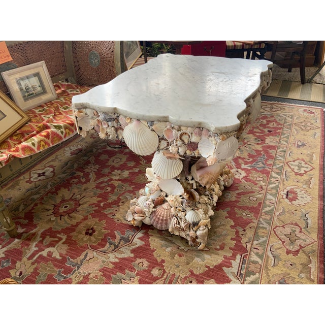 Shell encrusted table with marble top. Shells have been applied to wood finish of table. Marble top rests on base.