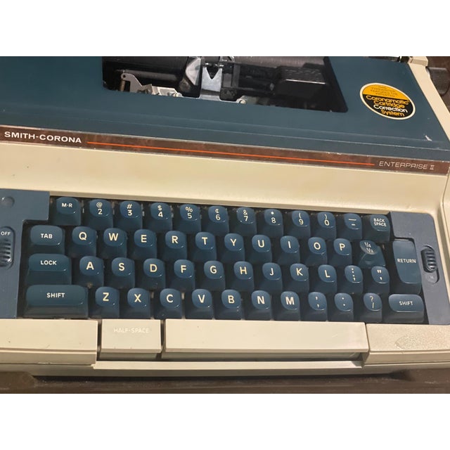 A vintage Smith-Corona Enterprise II electric typewriter featuring the original hard shell carrying case and Coronamatic...