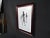 Unique minimalist painting of three stick figure people. This piece features a beautiful sloped wooden frame, glass and...