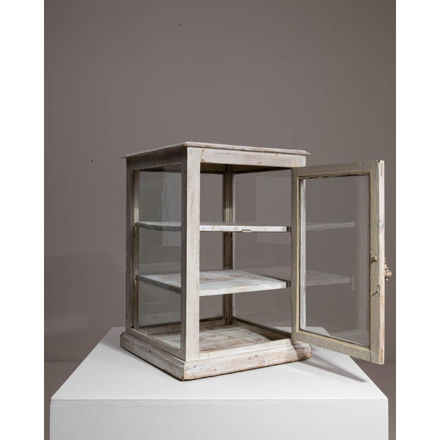 Here is a vitrine, its white painted wood, glass doors, small display case the first thing to catch the eye. The piece...