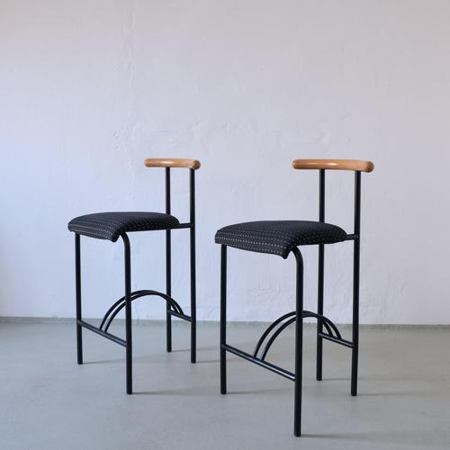 Pair of vintage bar stools featuring a minimalist black metal frame with curved footrests and sculptural wooden backrests....
