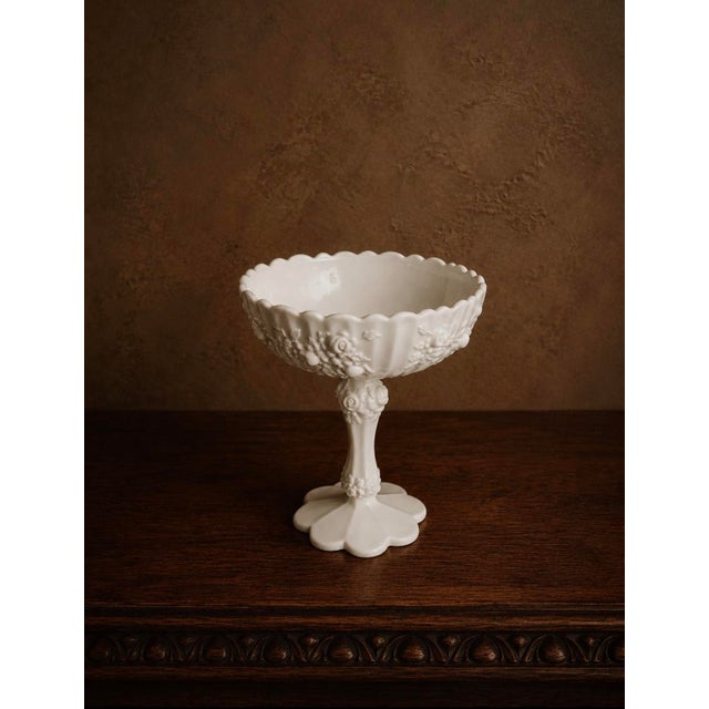 A lovely vintage milk glass compote with beautiful embossed detail, circa 1950s–60s. The wide scalloped bowl features...