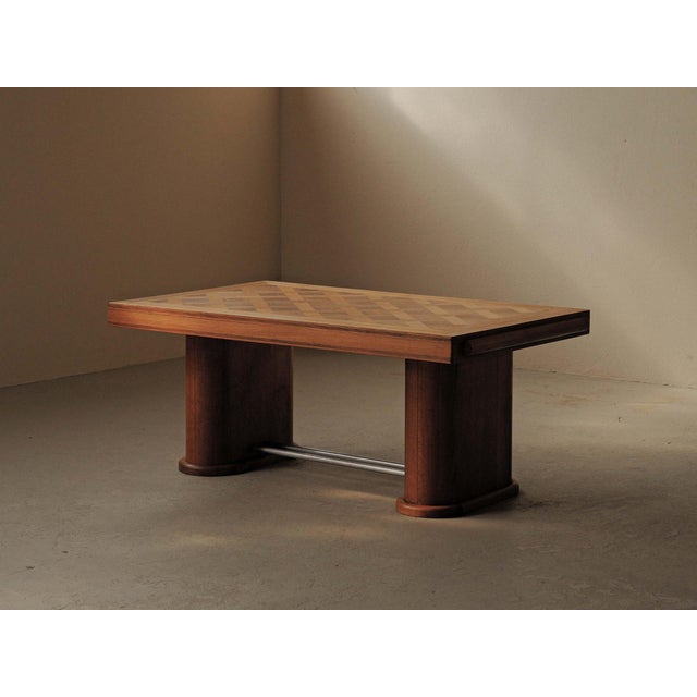 Art Deco table with a geometric marquetry top in oak and walnut, resting on two broad column-like supports joined by metal...
