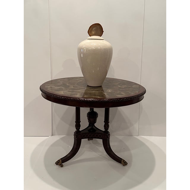 Stunning round center table having carved mahogany trio of splayed legs with center decorative urn. Top is a fascinating...
