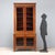 Empire walnut display cabinet. Glass-doored cabinet with sheet metal molding and carved geometric motif on the top. Base...