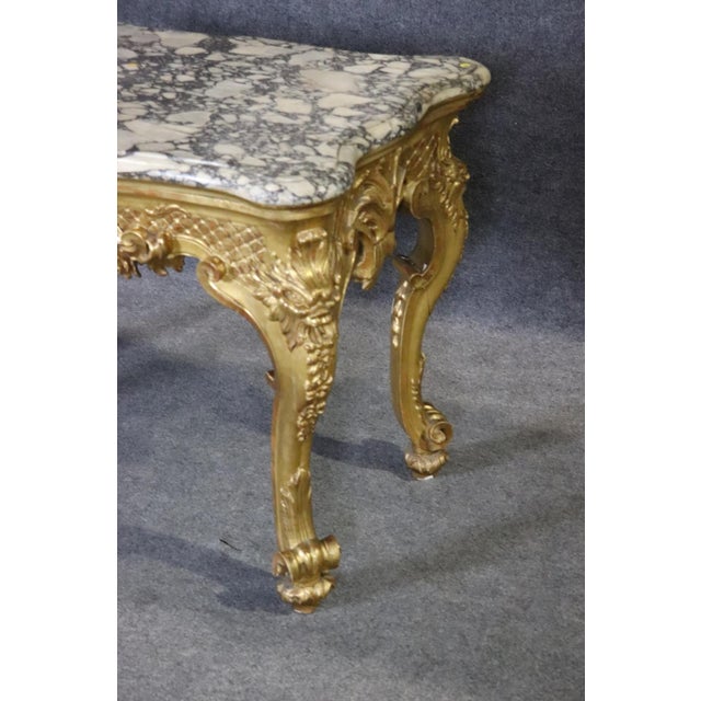 Measures: 34" h x 53 3/4" w x 31" d. This French Louis XV marble top giltwood center table carries the unmistakable rhythm...