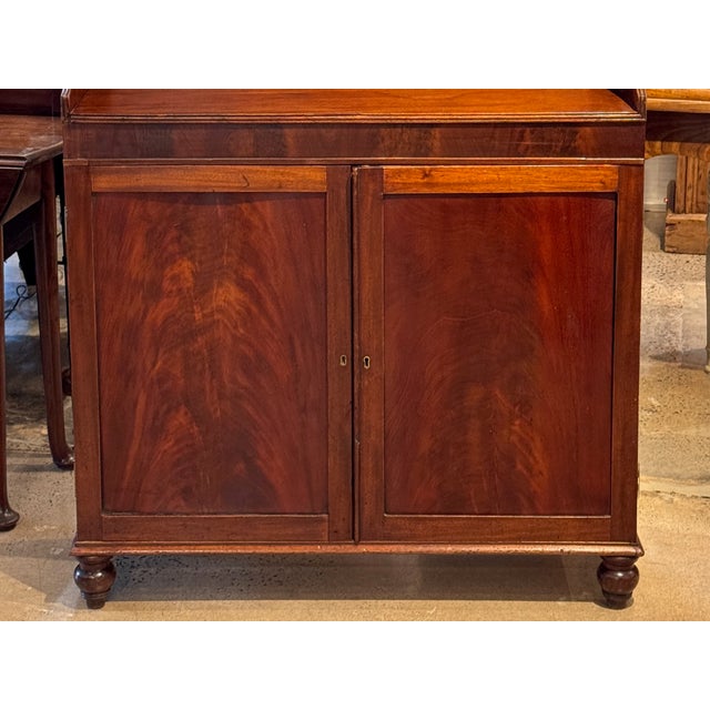 This English mahogany waterfall bookcase has a shaped crest rail above two open shelves, over a lower cabinet fitted with...