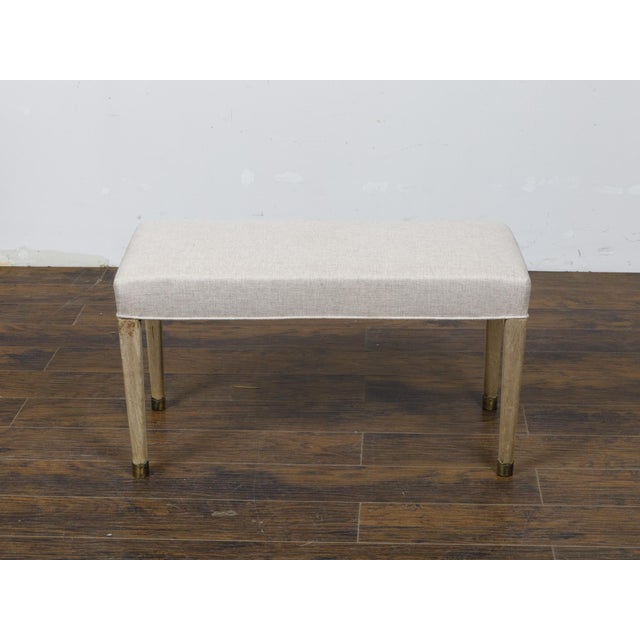 A French Art Deco bleached walnut bench from circa 1930 with brass feet and new custom linen upholstery. This exquisite...