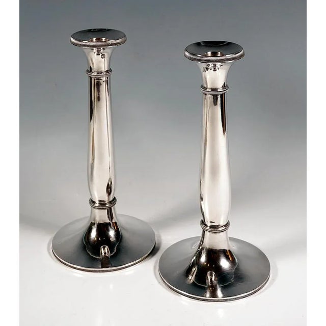 Two elegant, simple early Biedermeier silver candle holders on a round stand with a slightly curved, smooth shaft, chased...