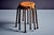 Round varnished plywood seats with visible grain and exposed metal rivets, supported by a brown tubular steel frame with...