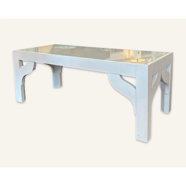 This Dorothy Draper style white coffee table is enameled wood with a glass top. The coffee table is from the legendary...