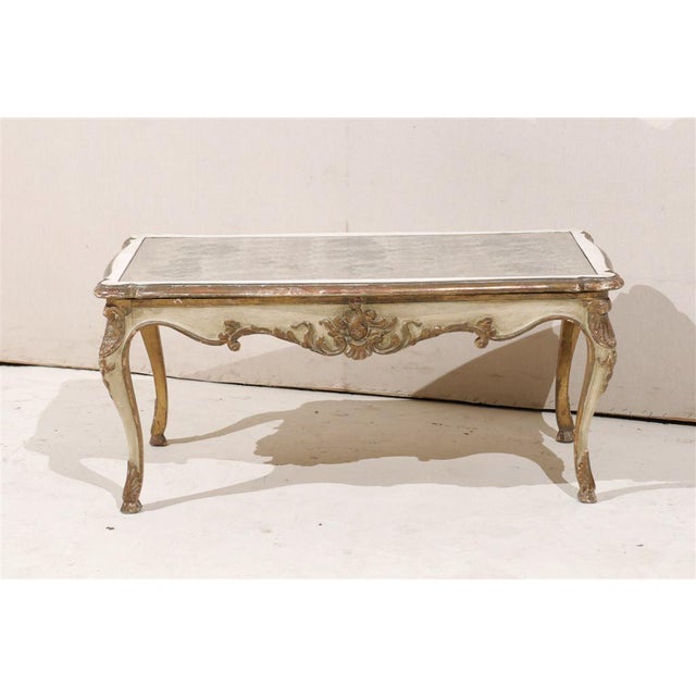 A French Louis XV style coffee table from the mid 20th century. This exquisite coffee table features an antiqued and...