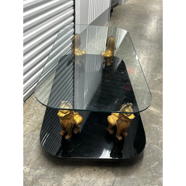 Very unique coffee table with high gloss black base, gold metal foo dogs supporting a thick glass top.